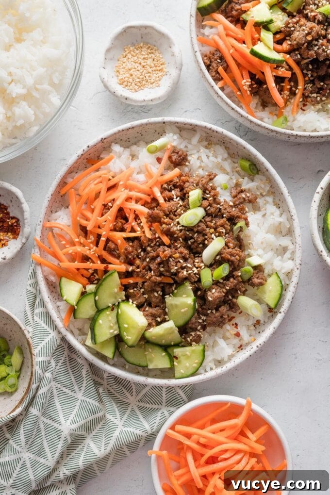 Countertop set with two bowls of Korean-inspired ground beef and rice topped with fresh veggies and toasted sesame seeds.