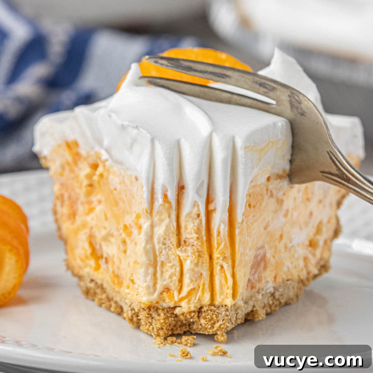 A thick slice of orange Tang pie with Cool Whip on top and mandarin orange garnish, sitting on a white plate as a fork presses into it.