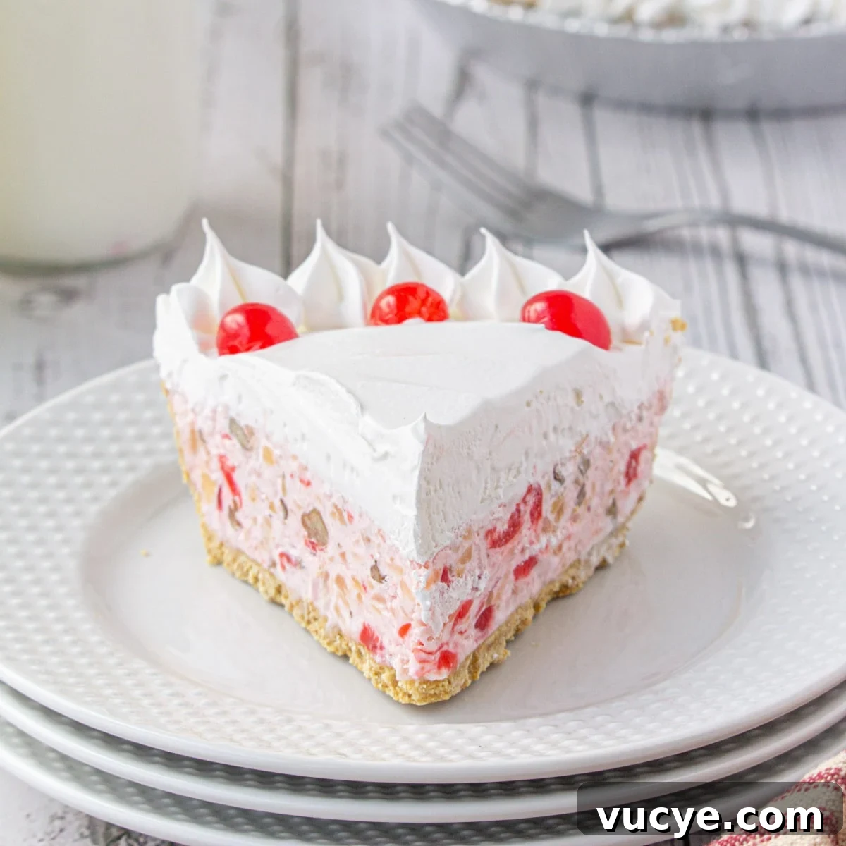 Closeup of a slice of pink cream pie with cherries on top on a white plate.