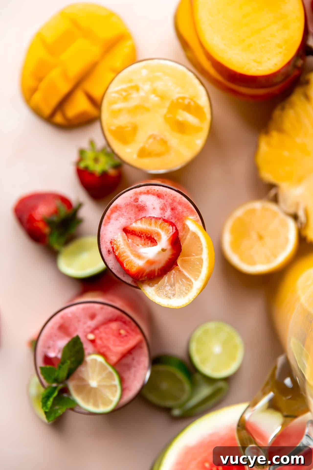 Overhead shot of cups of agua fresca on a counter surrounded by fruits.