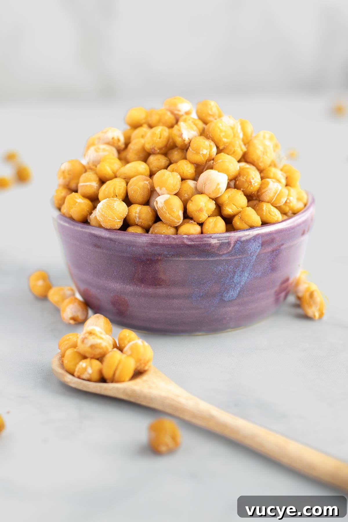 Crunchy roasted chickpeas in a purple bowl. A spoonful close up in front of the bowl.