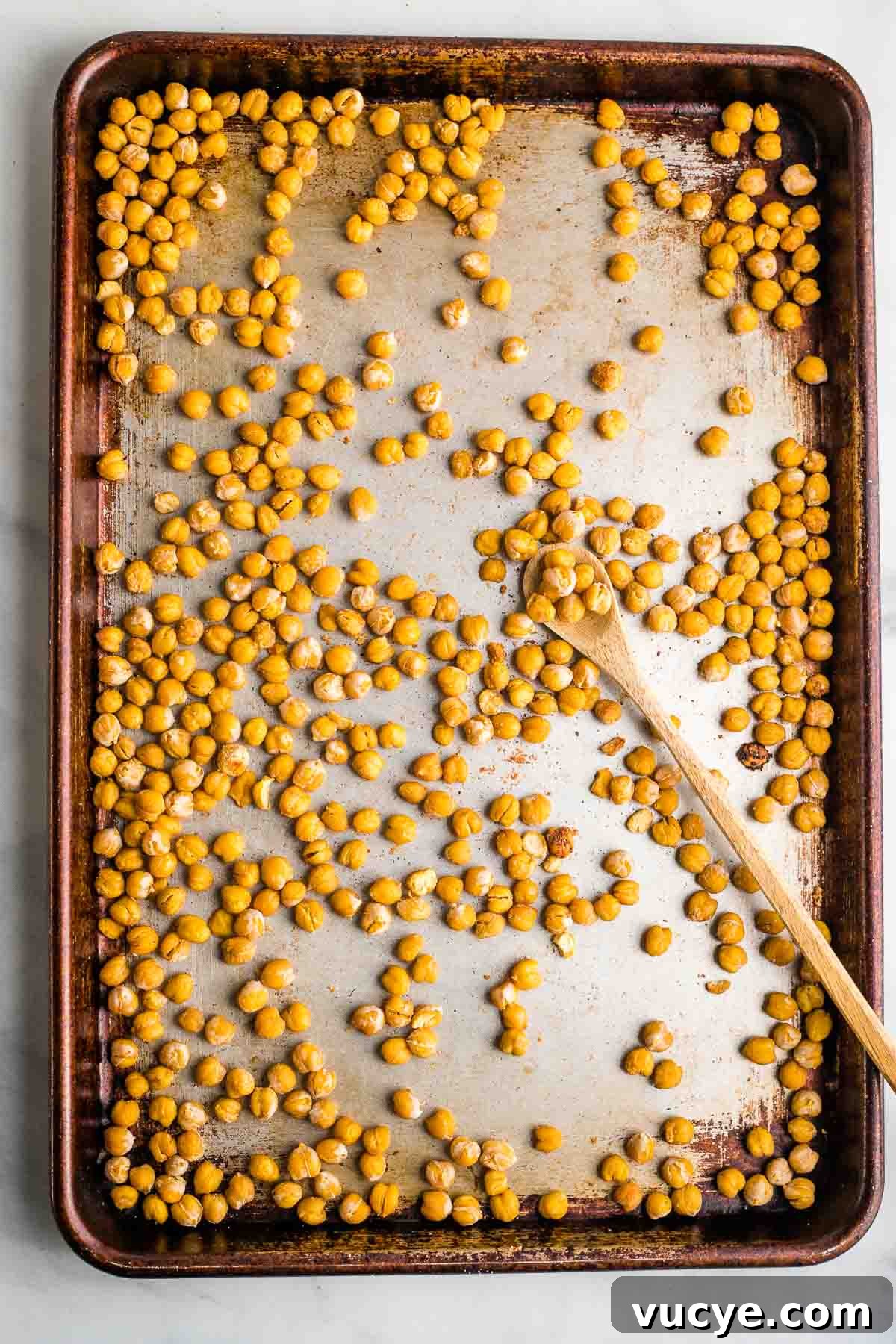 Crunchy roasted chickpeas on a baking sheet with spoon.