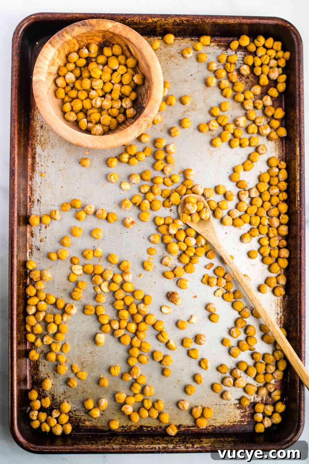 Crunchy chickpeas on a baking tray with a spoon placing them into a bowl.