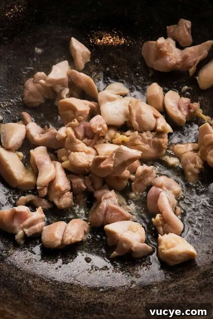 Chopped chicken thighs cooking in a pan.
