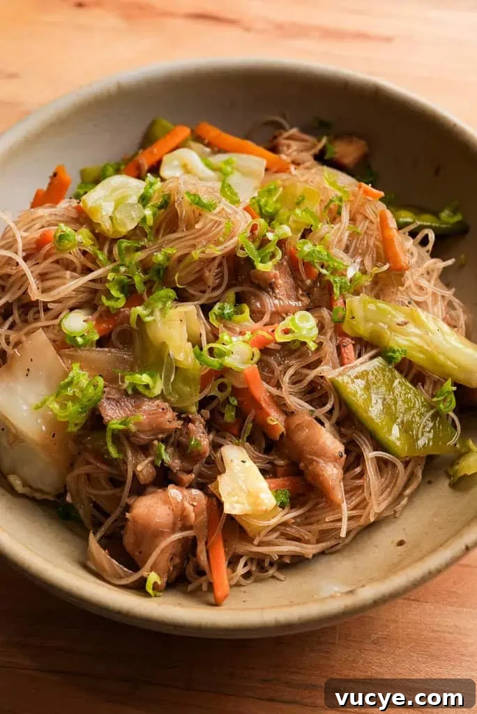 A bowl of pancit made with rice noodles, chicken thighs, and veggies.