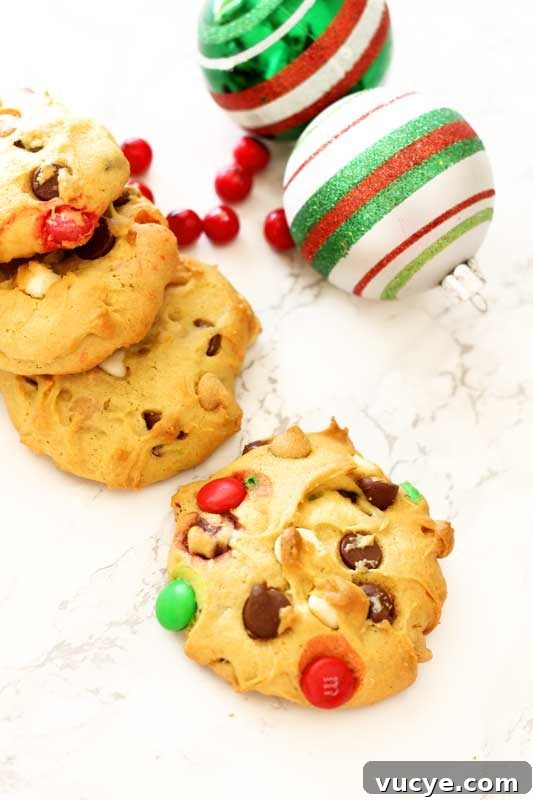 4 cookies sitting on a white marble table topped with M&Ms, Christmas calls on table with red cranberries.