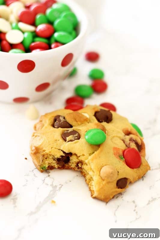 A boyfriend cookie with a bite taken out sitting on a white marble table, white and red polka dot dish filled with M&Ms on the side.