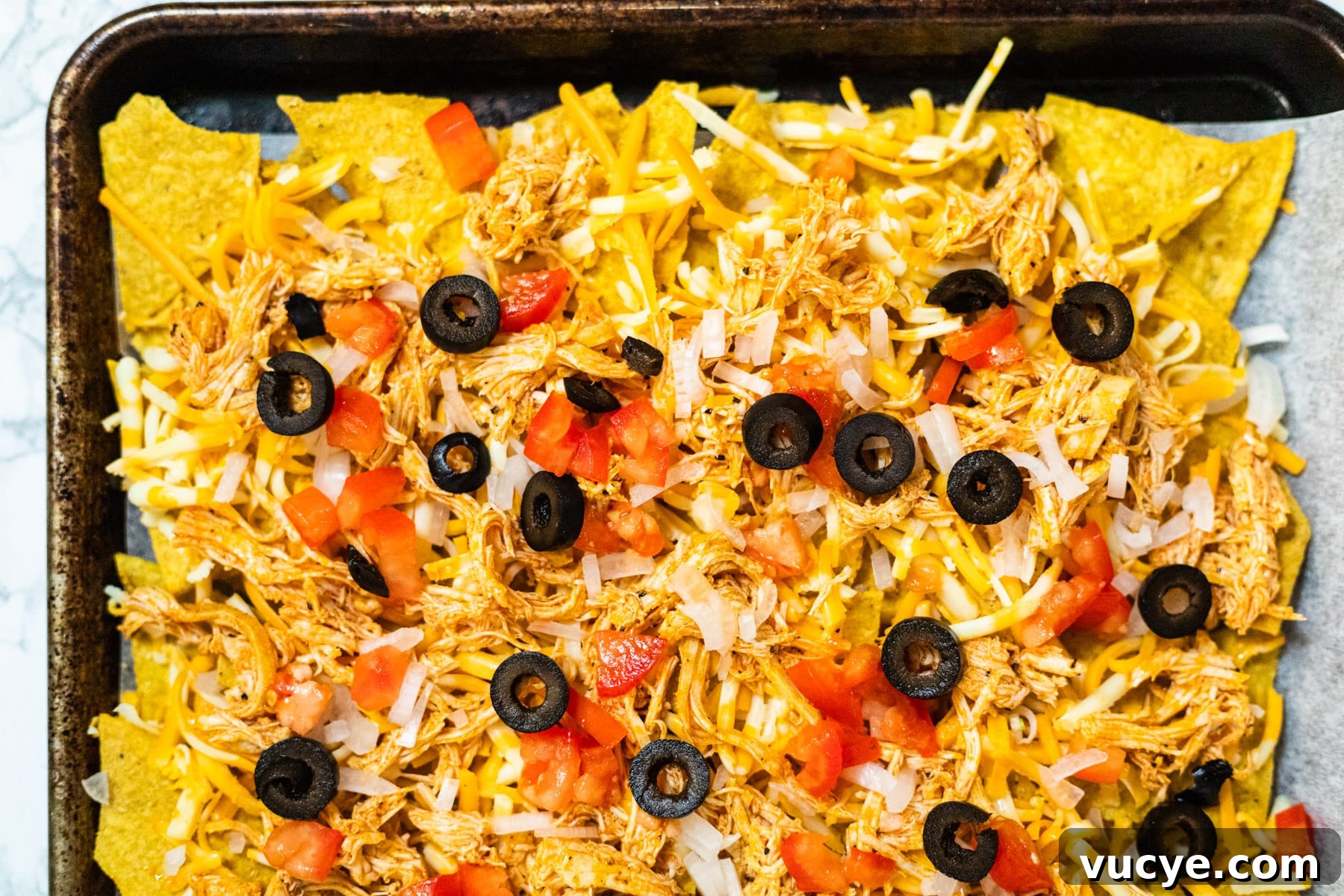 Nachos assembled on a sheetpan ready to bake