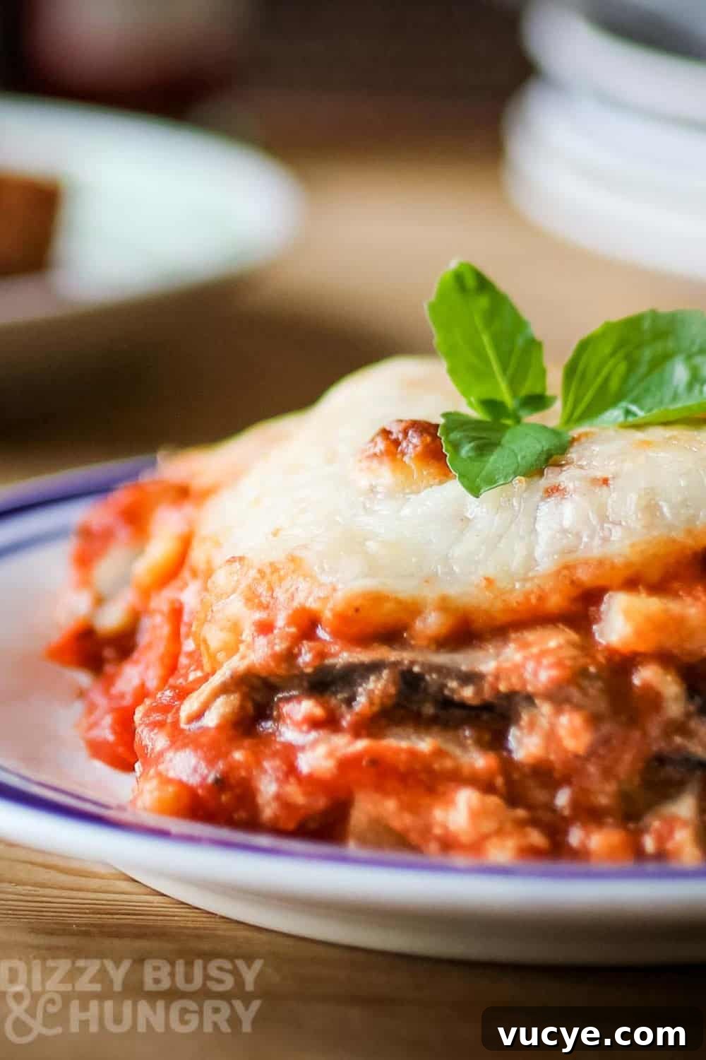 Side shot of eggplant polenta lasagna garnished with basil on a white and blue plate on a wooden table.