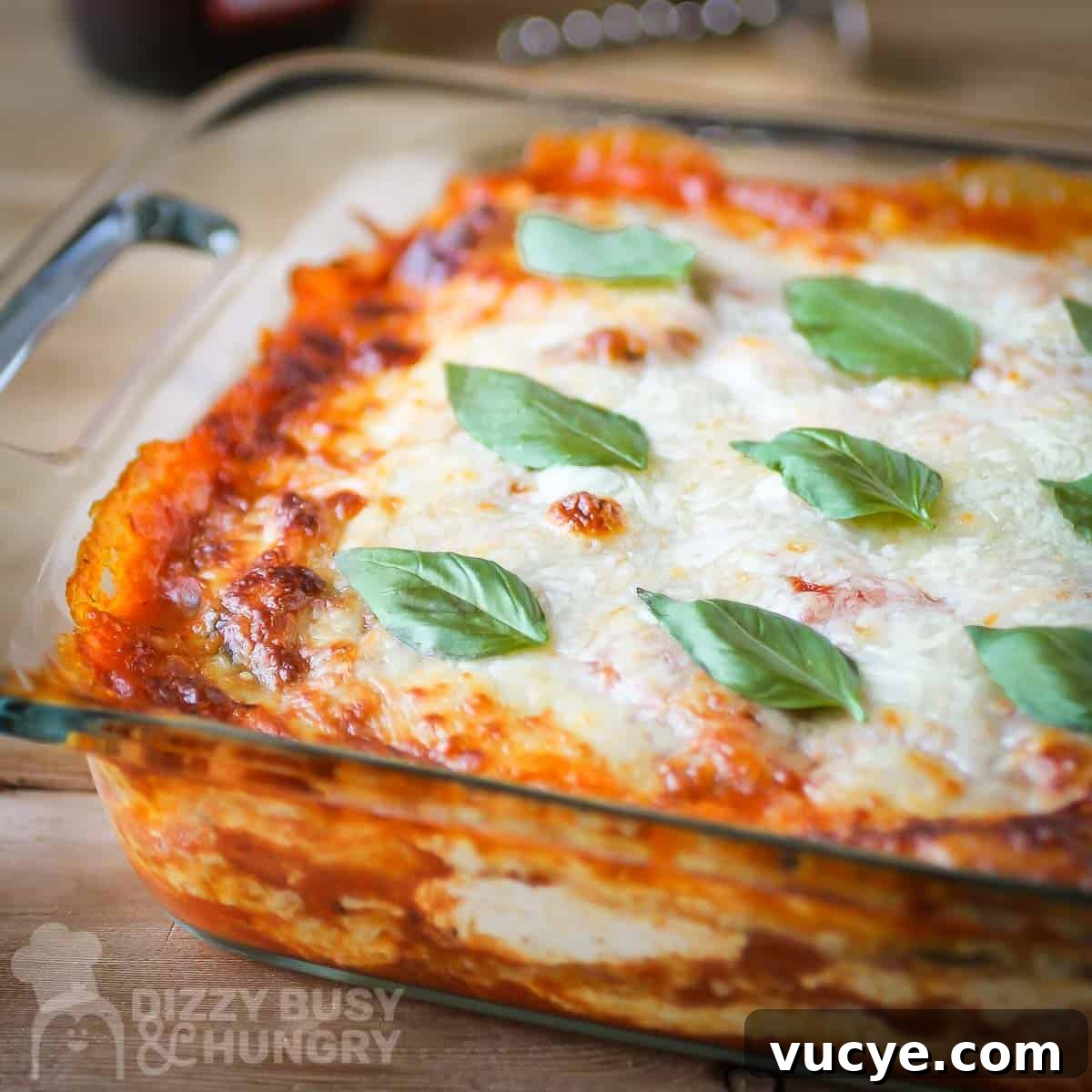 Side close up shot of polenta lasagna in a clear baking dish garnished with basil on a wooden table.